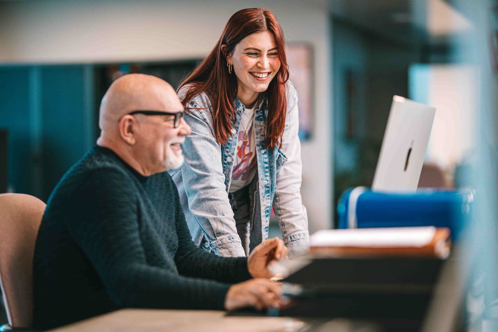 Zwei Kollegen lachen gemeinsam an einem Schreibtisch, während sie am Computer arbeiten
