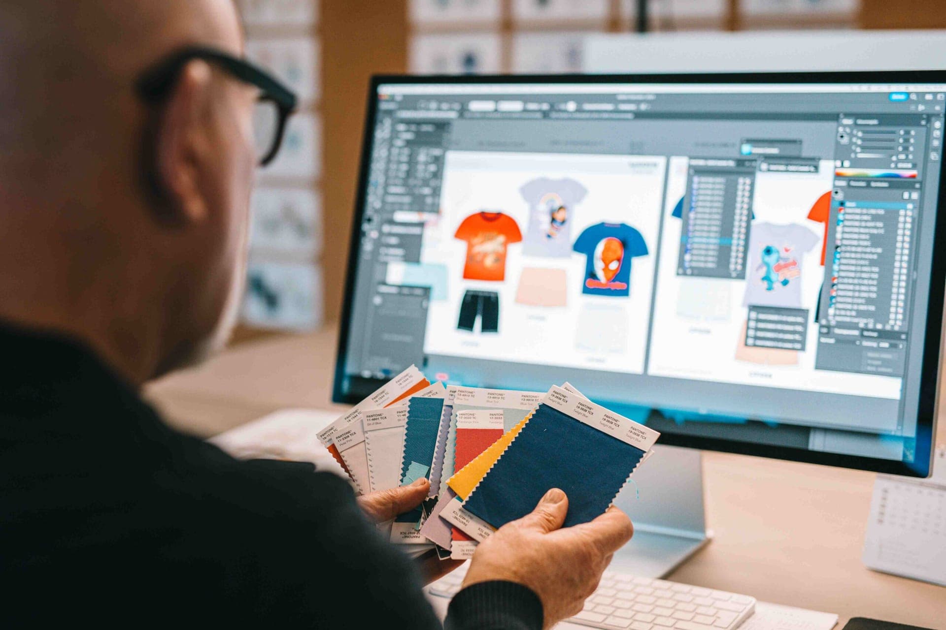 Styliste tenant des échantillons de tissu Pantone devant un écran affichant des modèles de t-shirts enfant sous licence