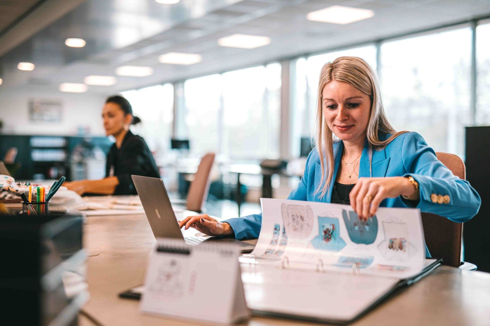 Styliste feuilletant un classeur de fiches de modèles de vêtements à côté d'un ordinateur portable