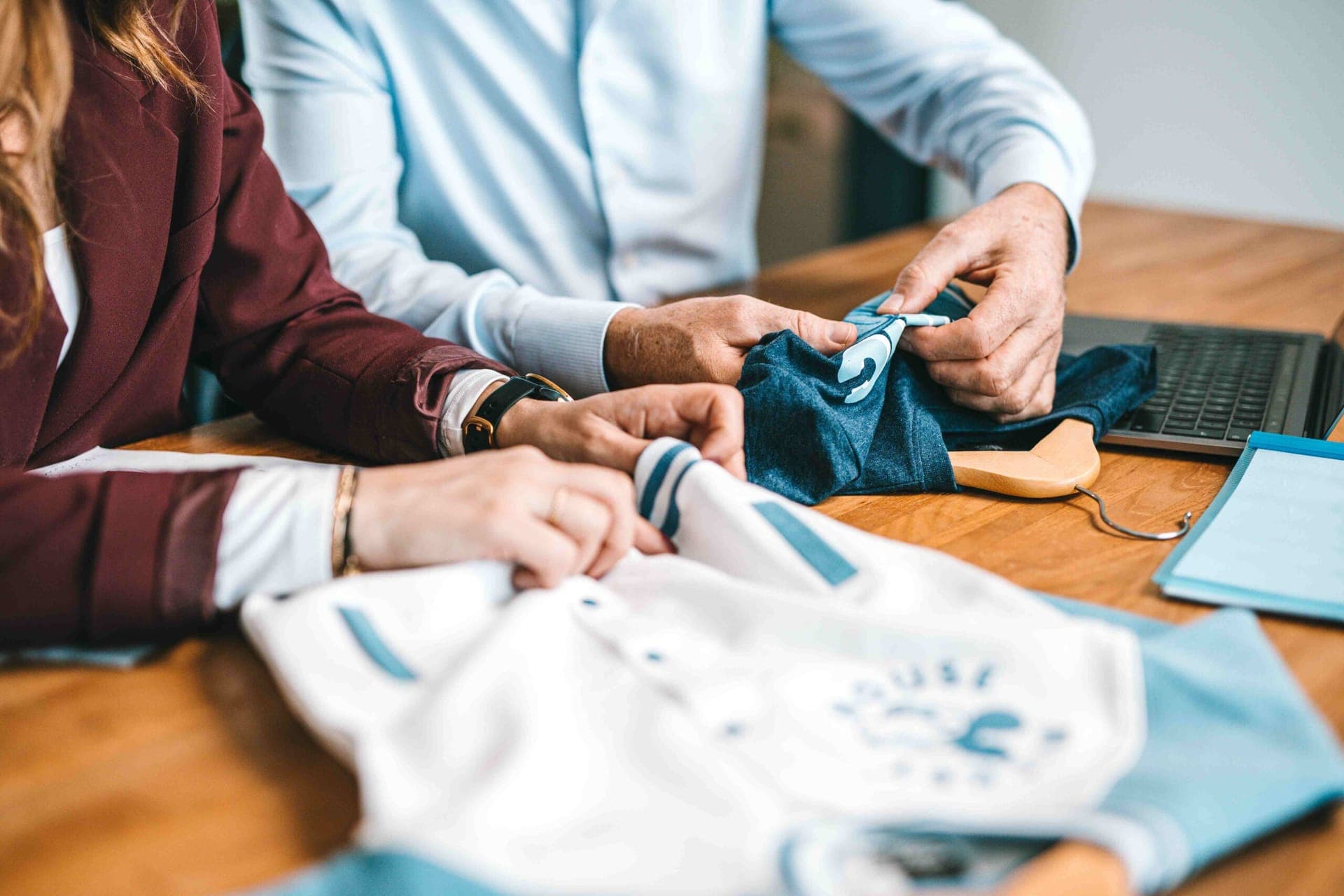 Colleagues examining garment samples: a white varsity jacket and a blue t-shirt