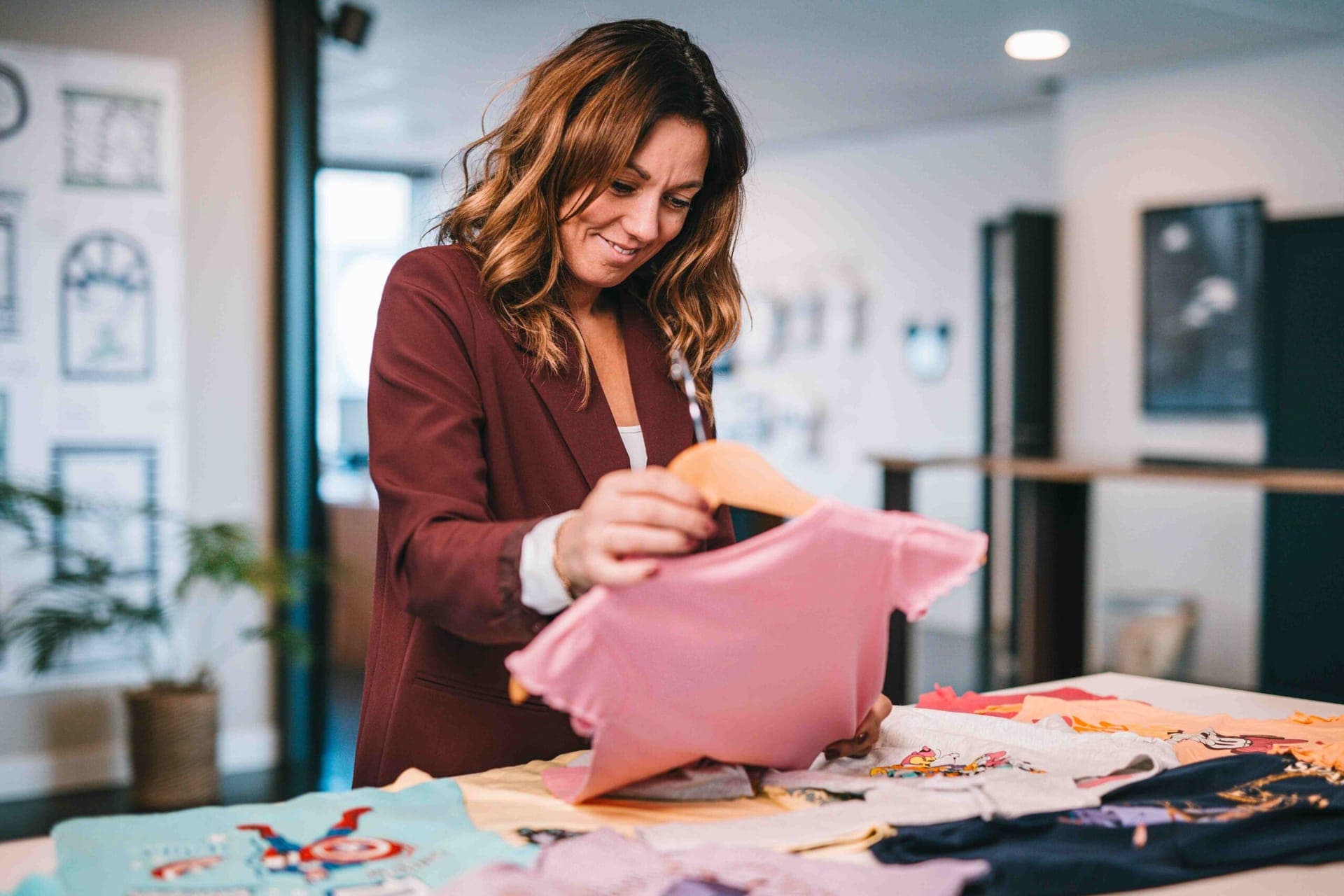 Une collègue choisit un t-shirt rose parmi des t-shirts enfant sous licence posés sur une table