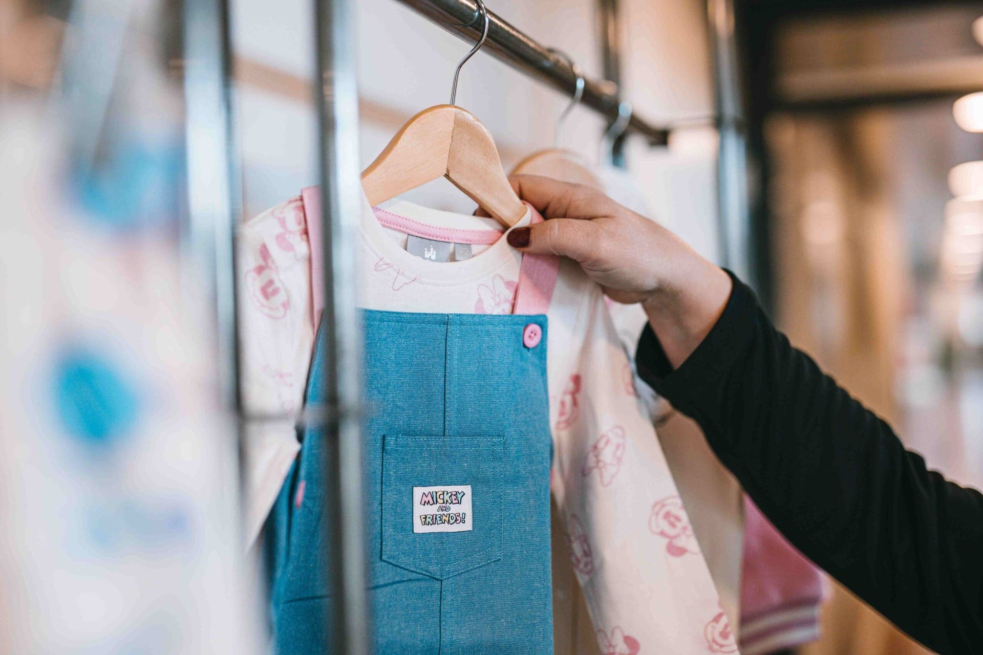 Gros plan sur une étiquette « Mickey and Friends » sur une robe-salopette en jean, à côté d'un haut à motif Minnie